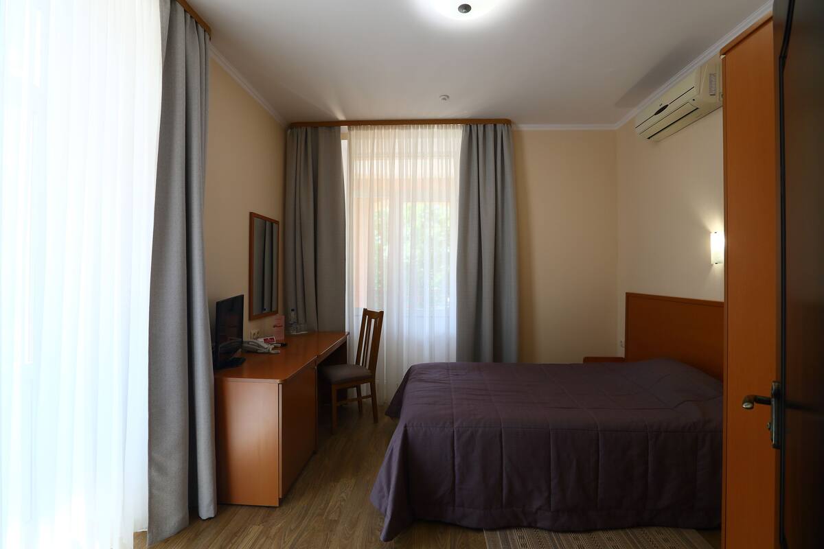 A hotel room with a bed, a desk with a chair, and a window with curtains.