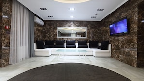 A modern lobby with a curved seating area, a large mirror, a flat-screen TV, and a marble wall. - Hotel Oberig Kiev (Kyiv)