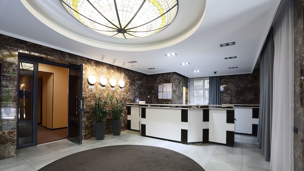 A modern reception area with a marble wall, a reception desk, a large circular carpet, and a ceiling light fixture. - Hotel Oberig Kiev (Kyiv)