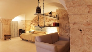A cozy room with a bed, a sofa, and a stone wall. There is a shelf with various items and a hanging light fixture. - Palazzo Camarda (Ceglie Messapica)