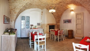 A stone-walled dining area with a fireplace, white furniture, and a chandelier. - Palazzo Camarda (Ceglie Messapica)