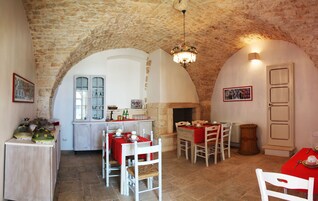 Comedor con paredes de piedra, chimenea, muebles blancos y una araña.