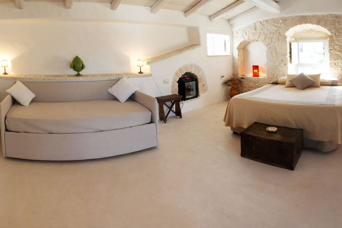 A cozy bedroom with a curved sofa, a bed, a small table, and a TV.