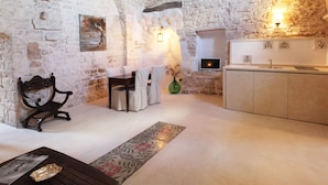 A rustic room with a stone wall, a wooden table with chairs, a small cabinet, and a decorative vase. - Palazzo Camarda (Ceglie Messapica)