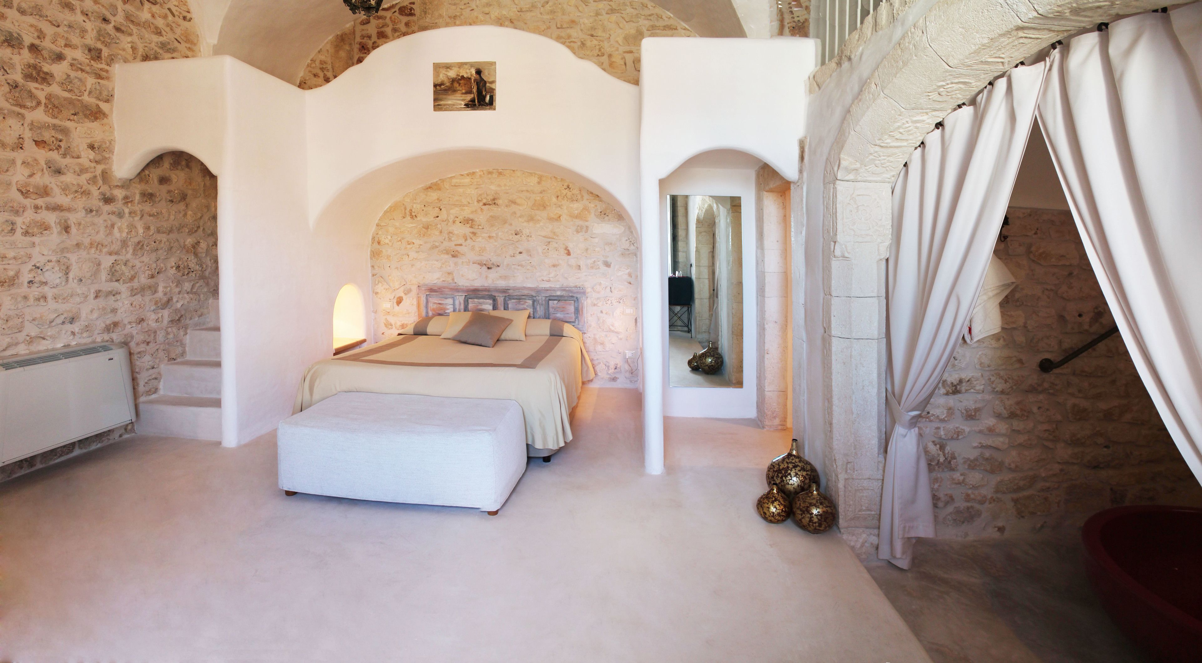 A bedroom with a stone wall, a bed, a mirror, and a red bath tub.