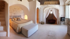 A bedroom with a large bed, a stone staircase, a red bathtub, and a small wooden dresser. - Palazzo Camarda (Ceglie Messapica)