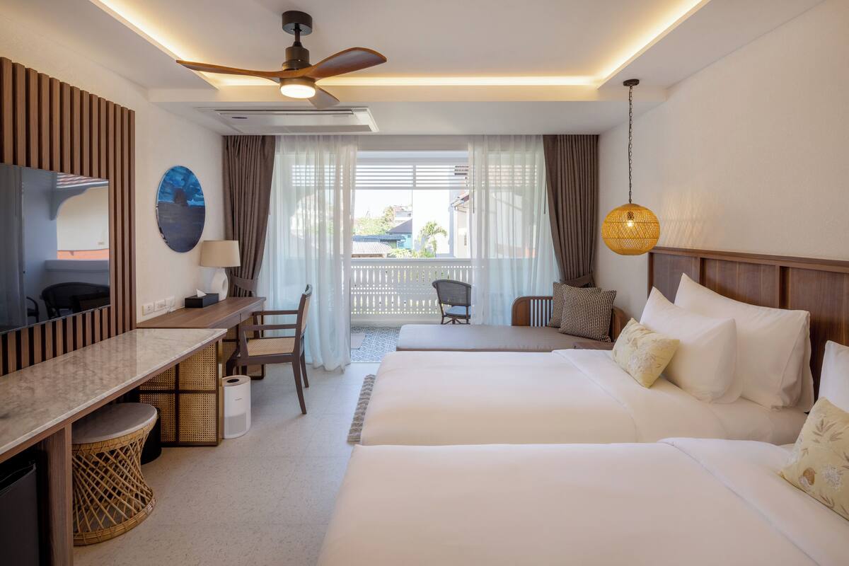 Ein Hotelzimmer mit Bett, Schreibtisch, Stuhl und einem Balkon mit Vorhängen.