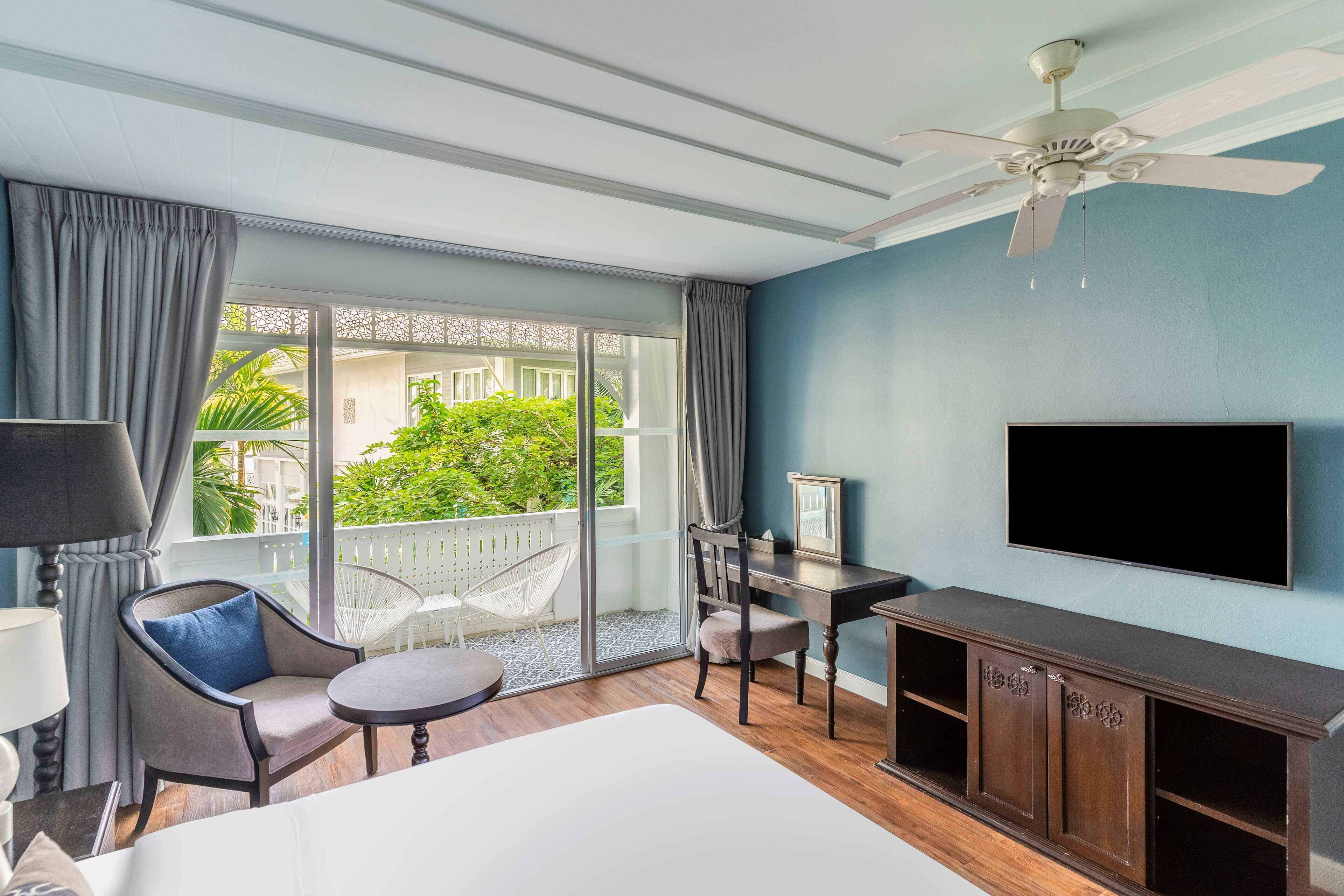 A hotel room with a bed, a desk, a chair, a TV, and a balcony with curtains.