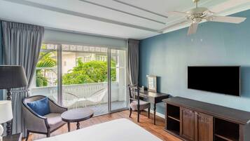 A hotel room with a bed, a desk, a chair, a TV, and a balcony with curtains.