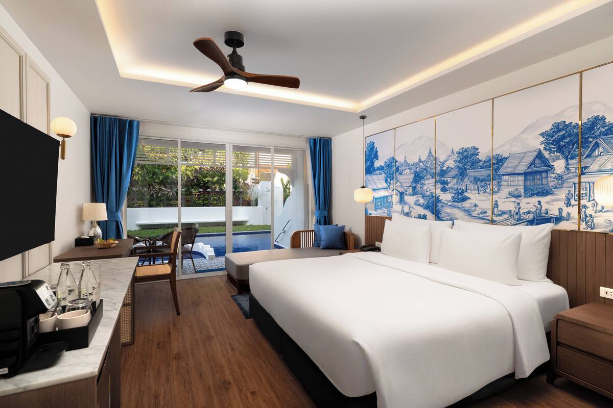 Ein Hotelzimmer mit einem großen Bett, einem Schreibtisch mit Kaffeemaschine, einem Fernseher und Blick auf einen Pool und Grünflächen.