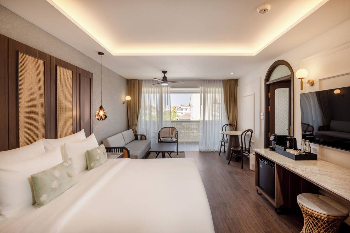 Ein Hotelzimmer mit einem großen Bett, einem Schreibtisch, einem Sessel und einer Couch, sowie einem Balkon mit Blick.