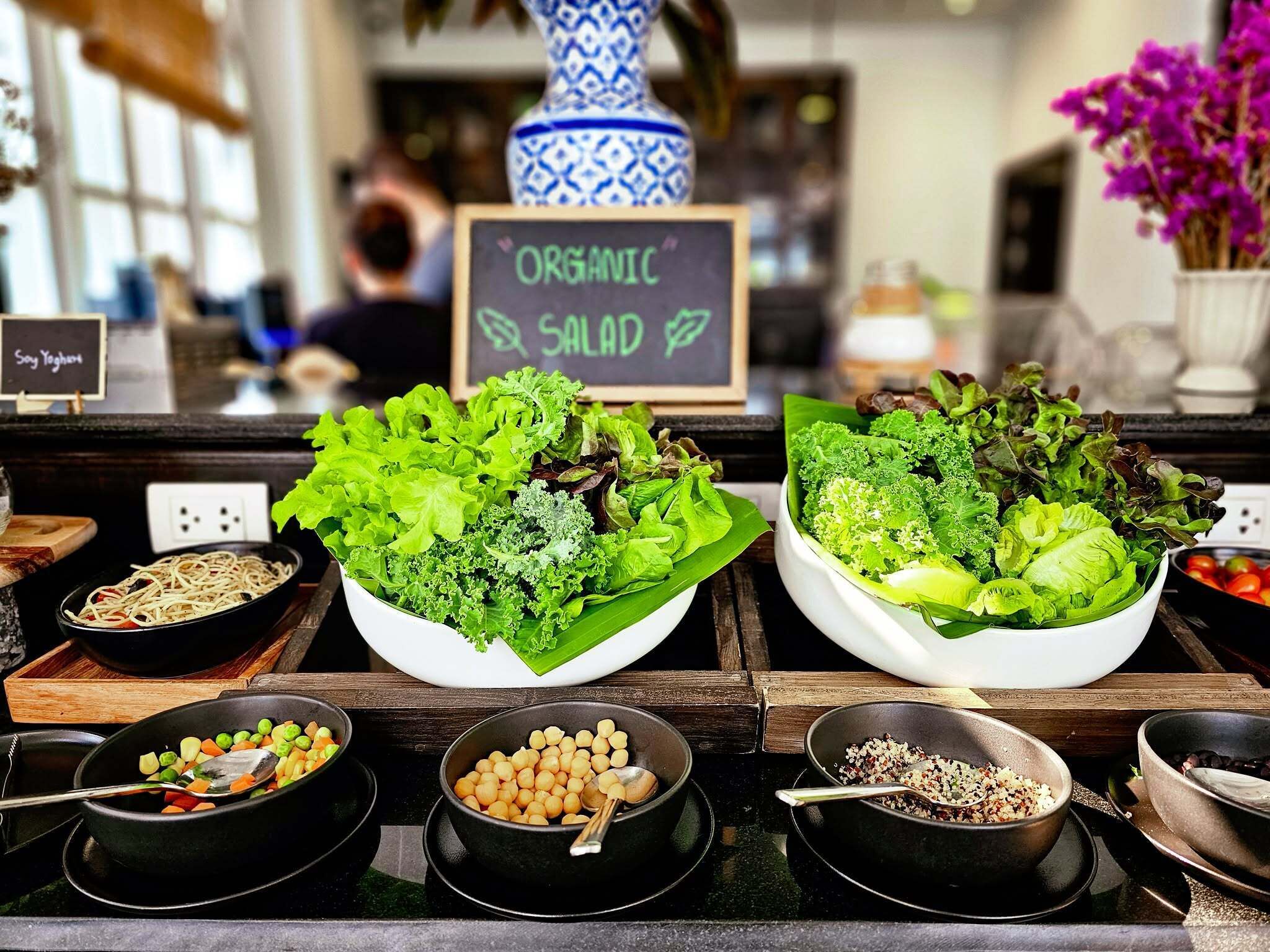 A salad bar with various greens and legumes, a chalkboard sign indicating 'ORGANIC SALAD', and a sign for 'Soy Yogurt'.
