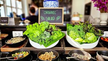 Una barra de ensaladas con diversas verduras y legumbres, un cartel de tiza que indica 'ORGANIC SALAD', y un letrero para 'Soy Yogurt'.