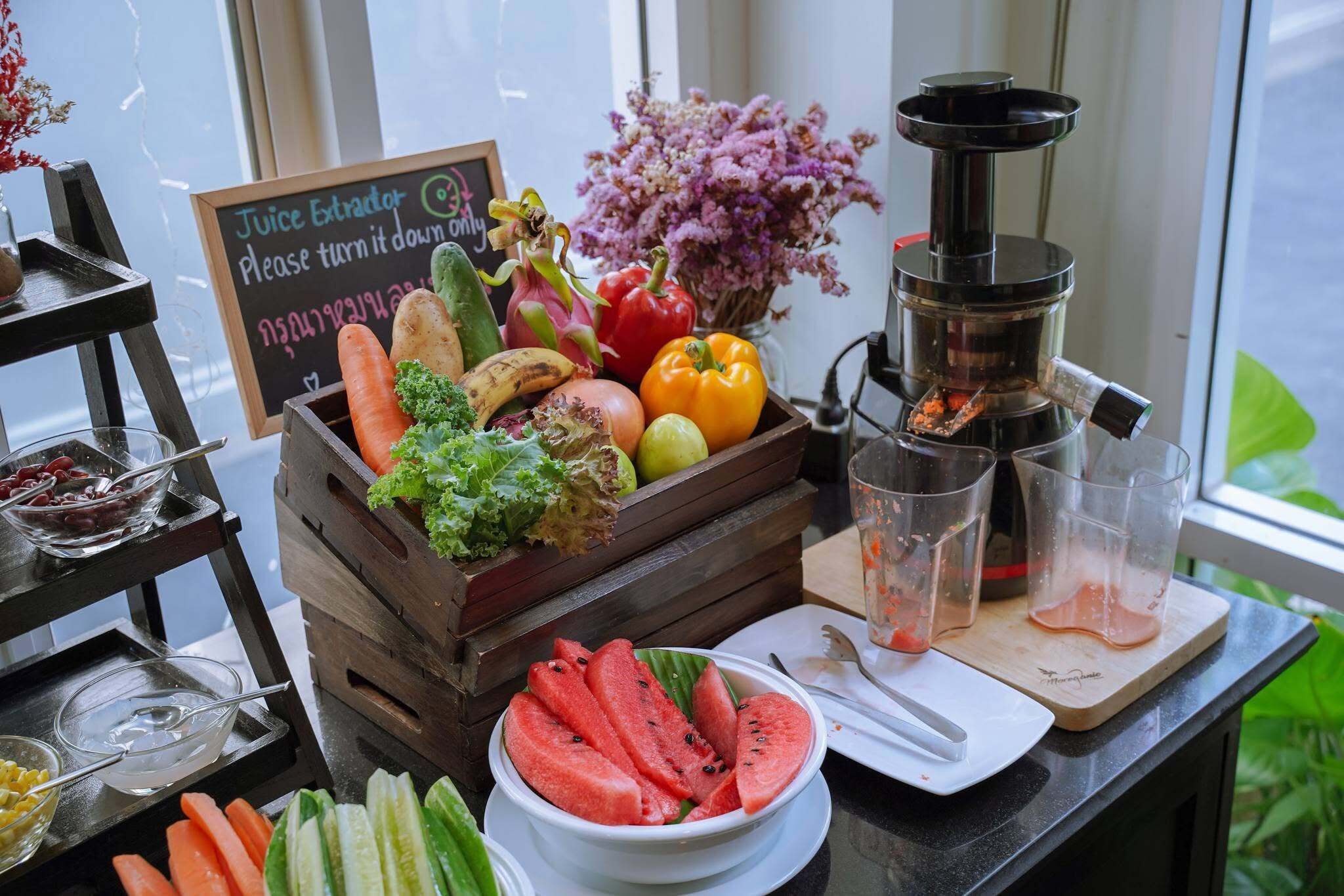 Estrattore di succo, frutta fresca, verdure e una ciotola con fette di anguria su un tavolo.