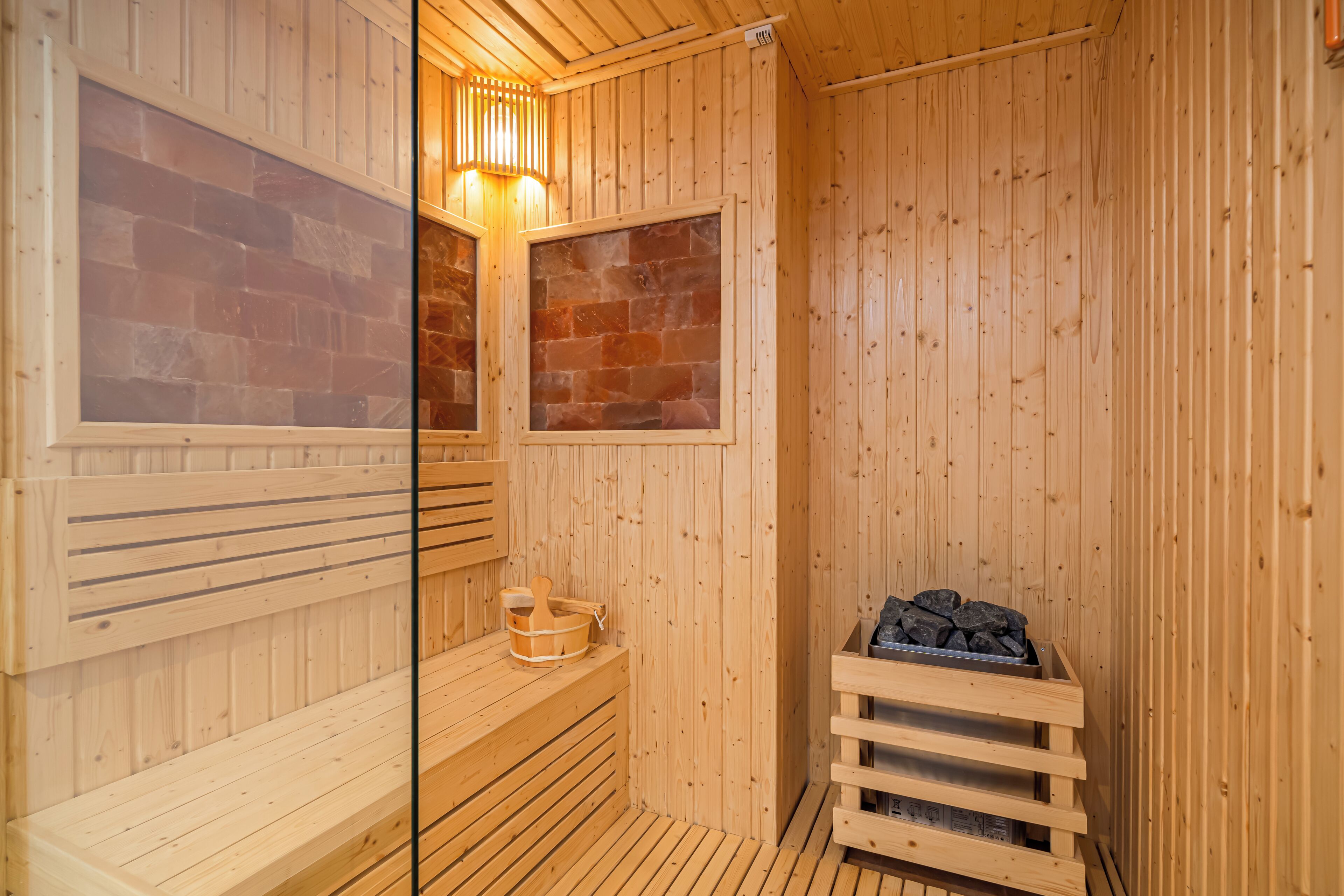 A wooden sauna with benches, a stone wall, and a wood-burning stove.