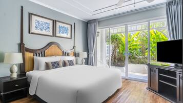 A hotel room with a large bed, a TV, and a balcony with a view of greenery.