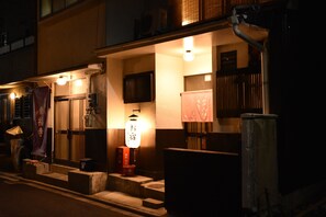 A traditional Japanese building with a wooden exterior, a small entrance with steps, and a lit lantern. - Oyado Tofukuji 2 (Kyoto)