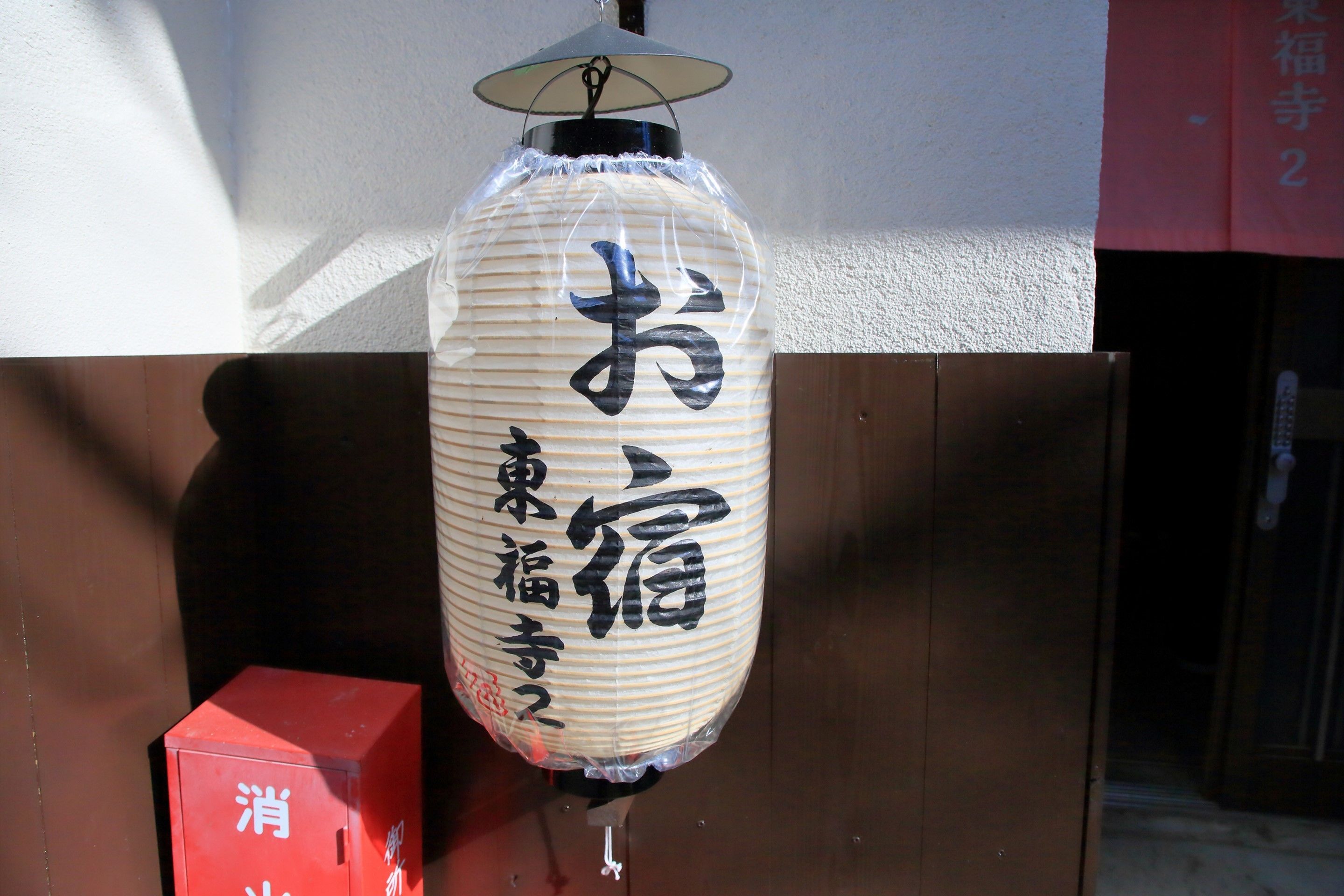 A traditional Japanese lantern with calligraphy, a red box with white text, and a wooden structure.