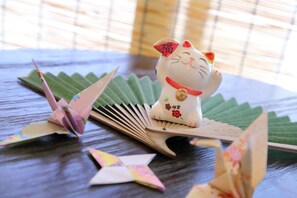 A decorative cat figurine on a table with origami figures and a fan.