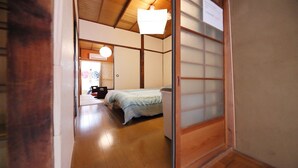 Perinteinen japanilaistyylinen huone, jossa on puulattia, raidallinen peitto sängyllä, liukuva shoji-paperiovi ja kattotuuletin.