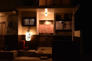 A traditional Japanese room with tatami flooring, a shoji screen, a hanging lantern, and a small table with a red container.