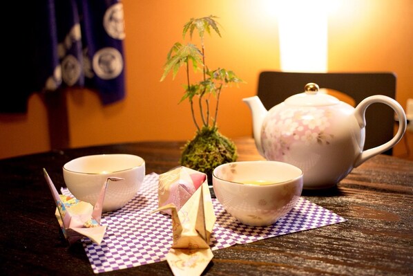 A table with two white cups, a teapot, and a small bonsai tree on a checkered placemat.