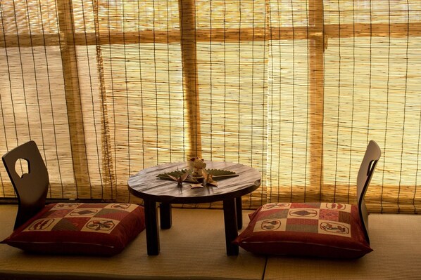 A room with a tatami mat floor, a round table with a decorative item, and two chairs with patterned cushions.