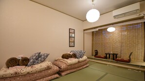 Tatami-mattoilla päällystetty huone, jossa on futon-patjoja, tyynyjä, pieni pöytä ja perinteinen japanilainen liukuovi.