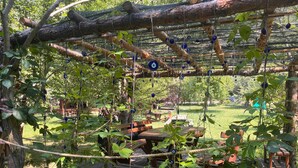 A rope bridge with blue charms hanging from it, surrounded by greenery and wooden structures. - Abant Yeşil Vadi (Bolu)