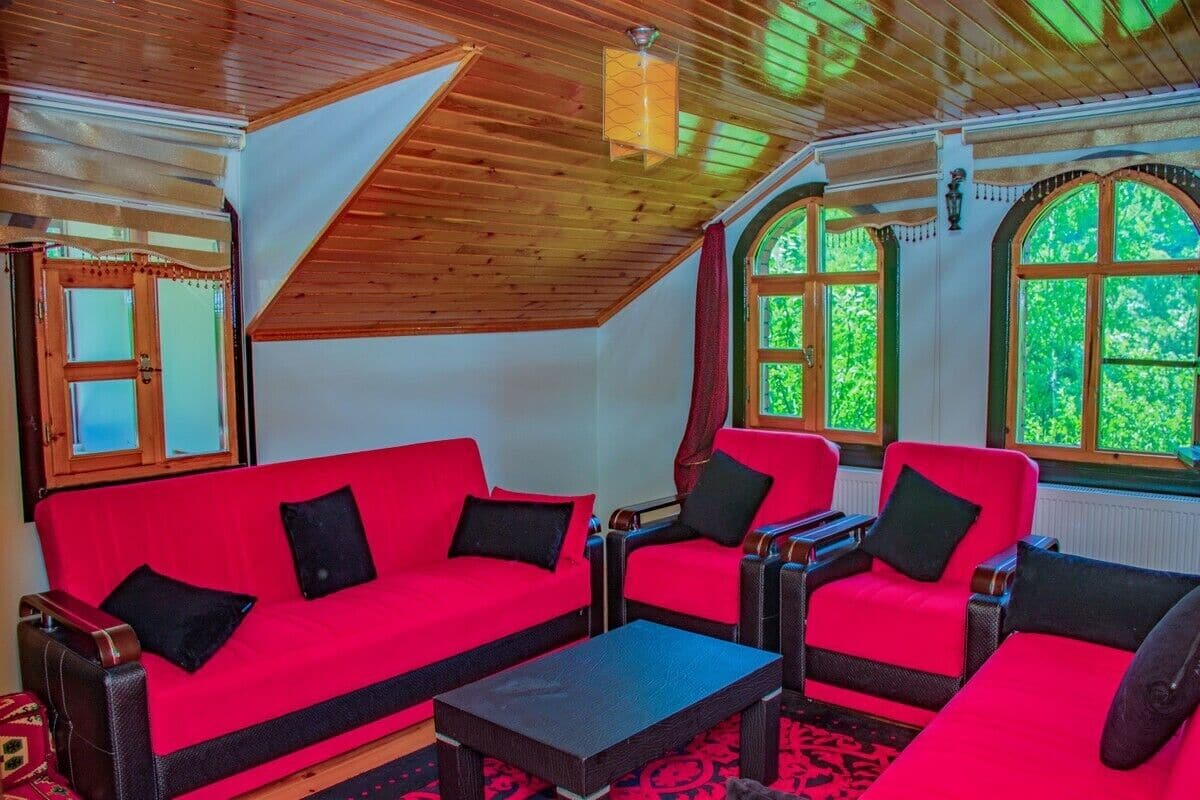 A room with a red sofa set, a small table, and large arched windows with greenery outside.