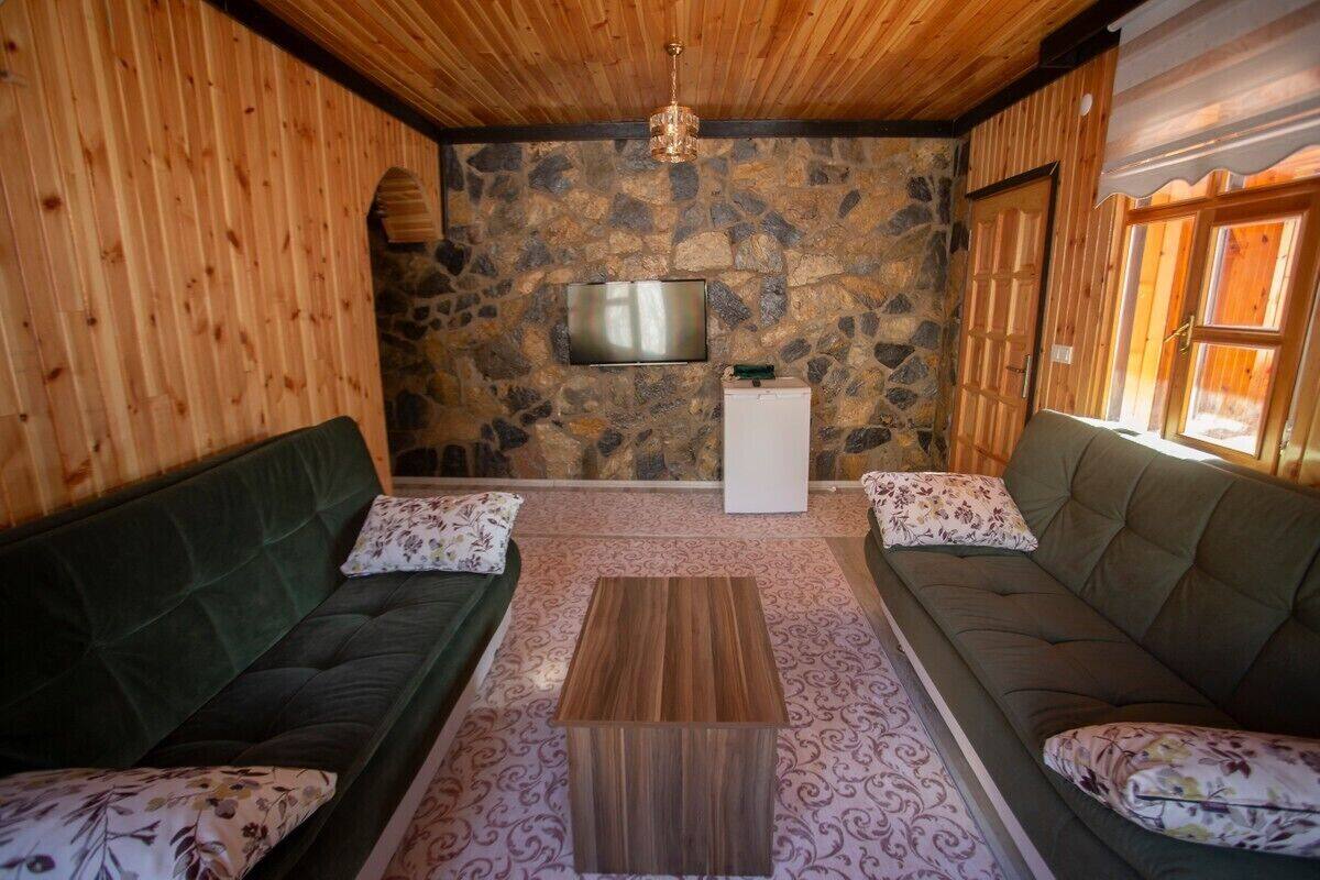 A cozy room with a stone wall, wooden ceiling, and two green sofas with floral cushions.