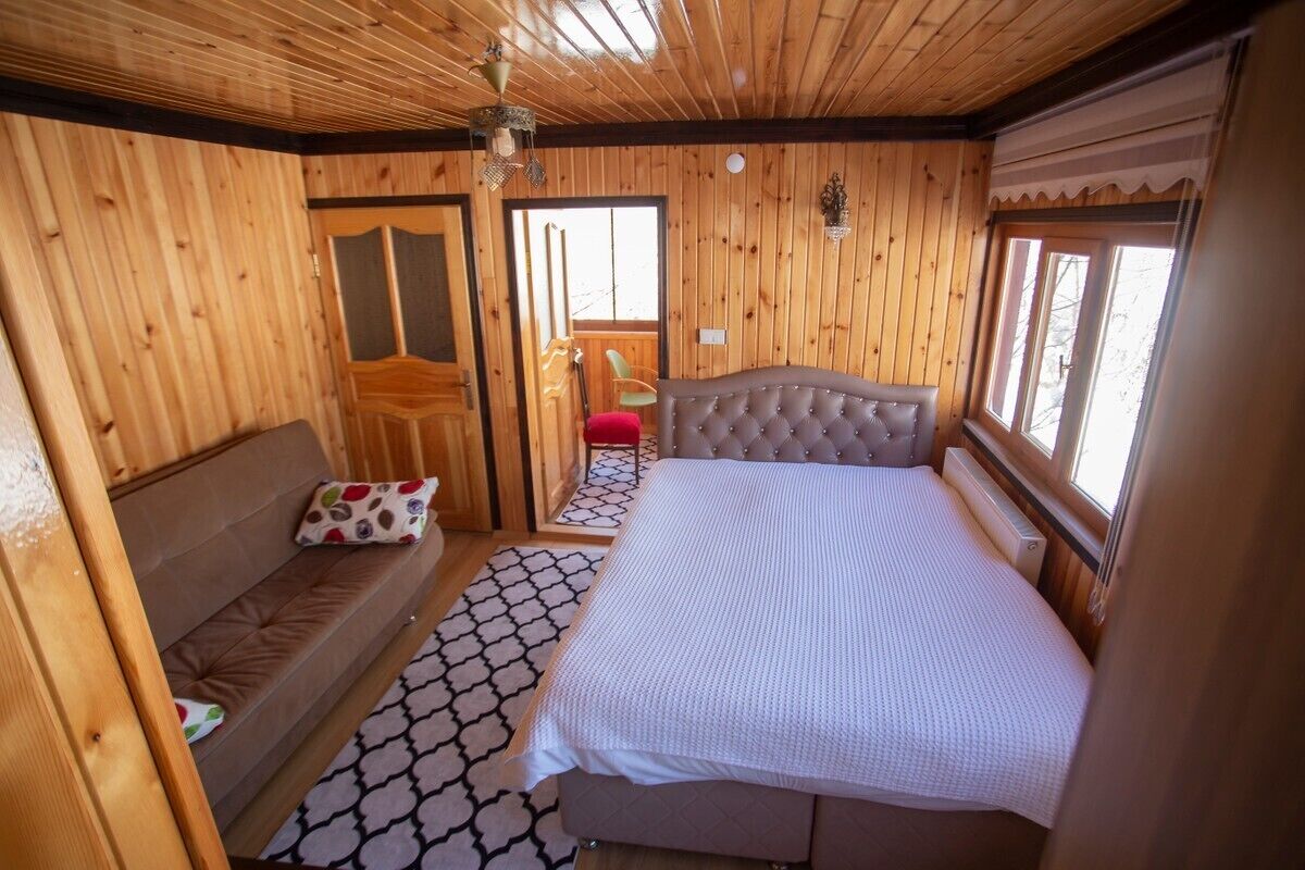 A wooden cabin room with a bed, a bench, a chair, and a window.