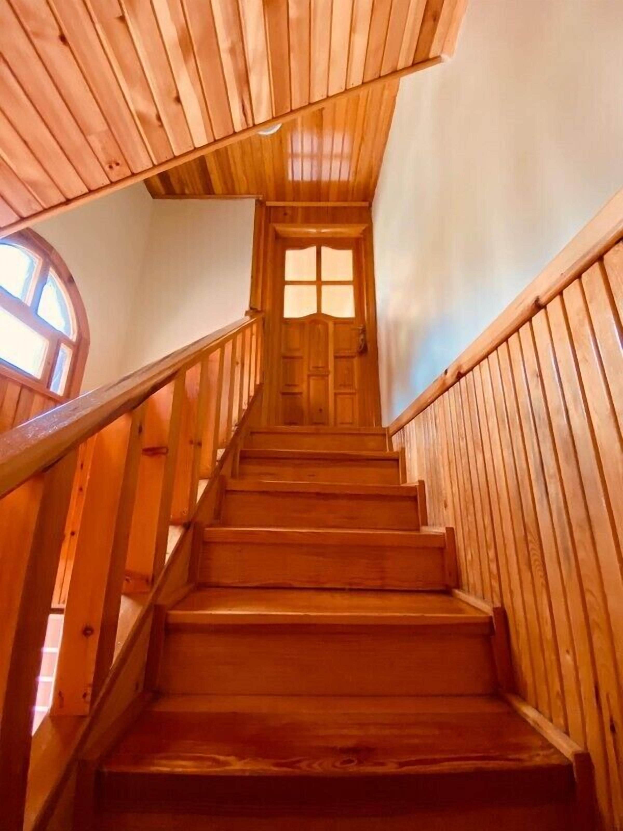 Una escalera de madera con barandilla que conduce a una puerta con ventanal.