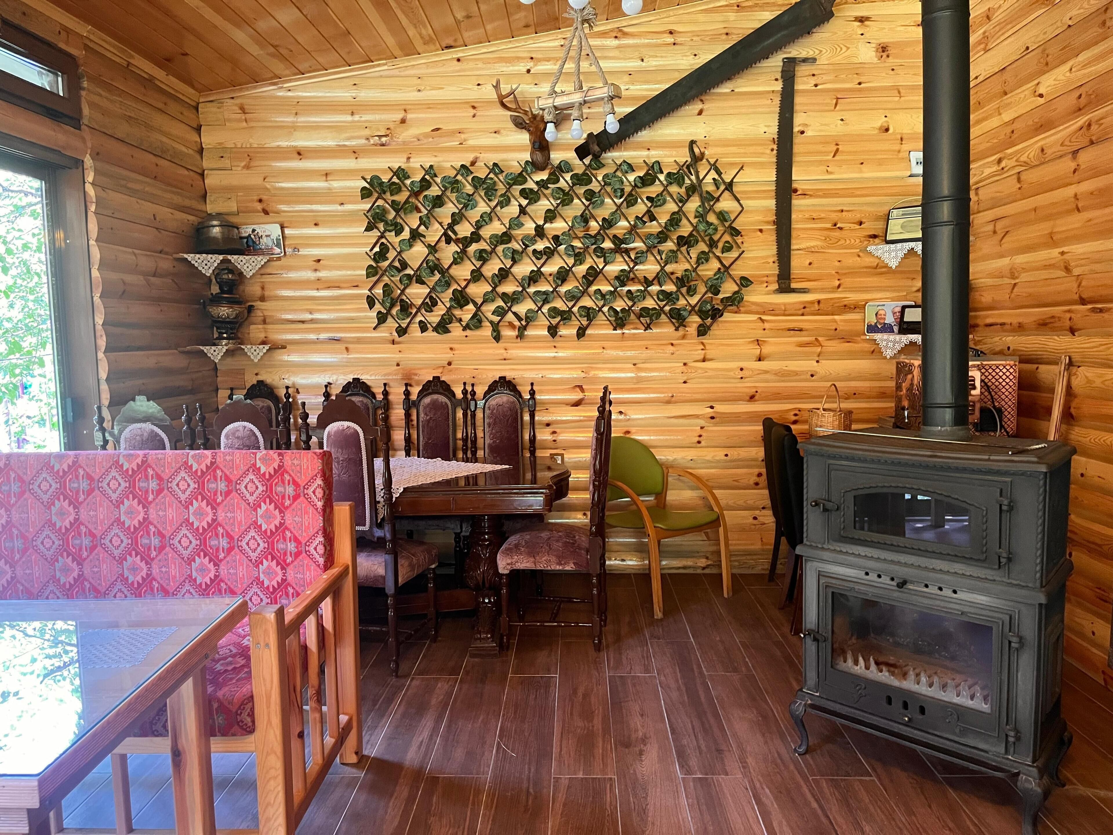 A wooden cabin interior with a dining table, chairs, a fireplace, and a wall-mounted plant grid.