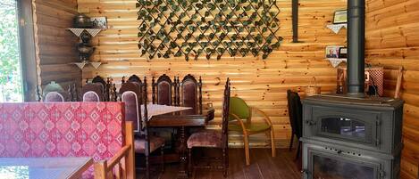 A wooden cabin interior with a dining table, chairs, a fireplace, and a wall-mounted plant grid.