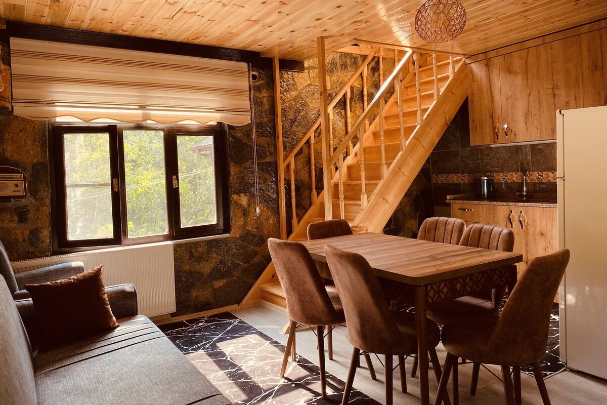 A wooden interior with a dining area, stone walls, and a staircase.