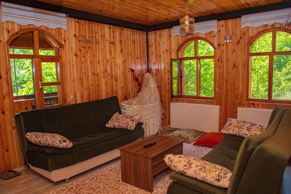 A cozy room with wooden walls, a green sofa, a wooden coffee table, and large windows with views of greenery.