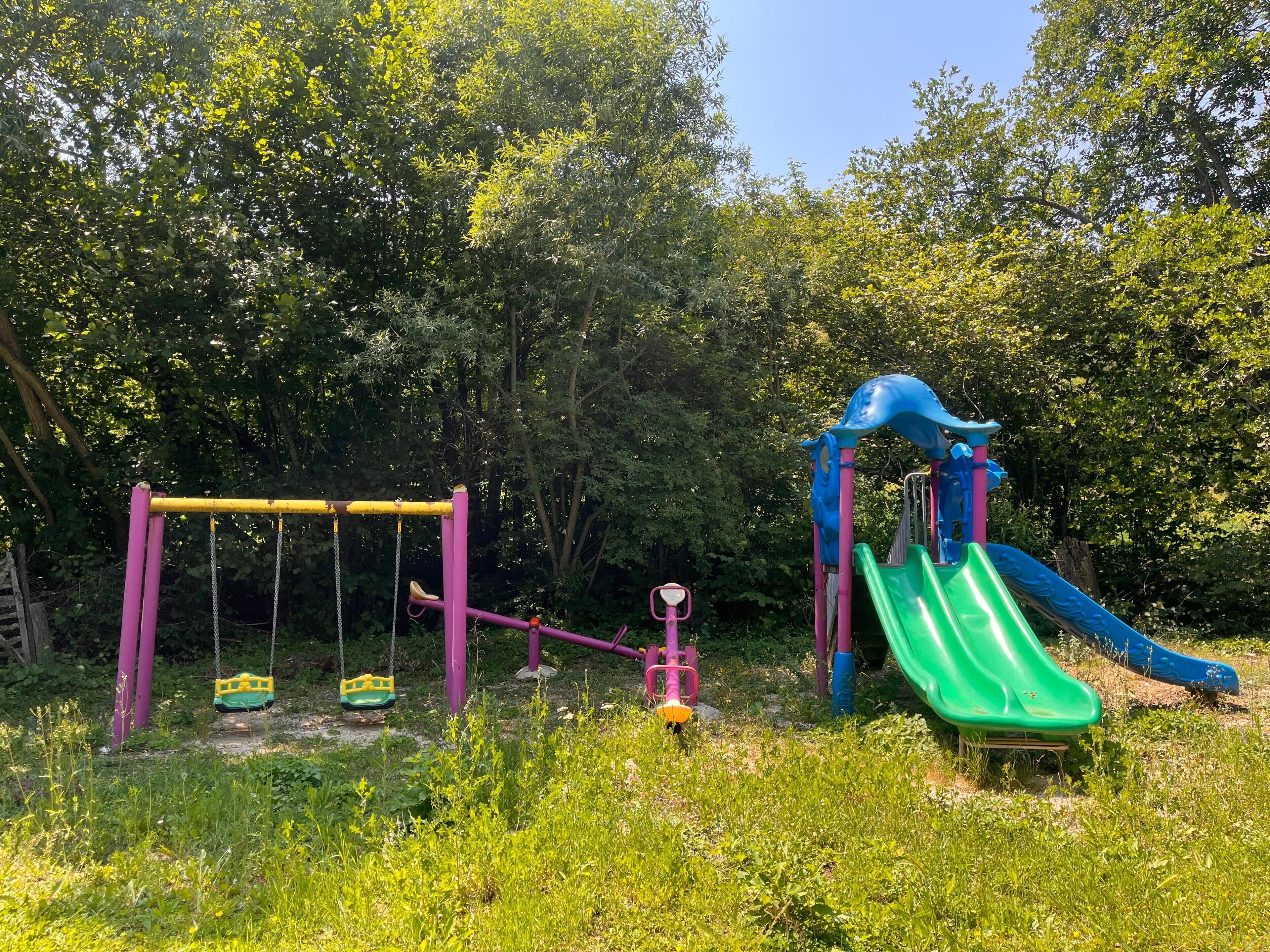 A playground with swings, a seesaw, and a slide.