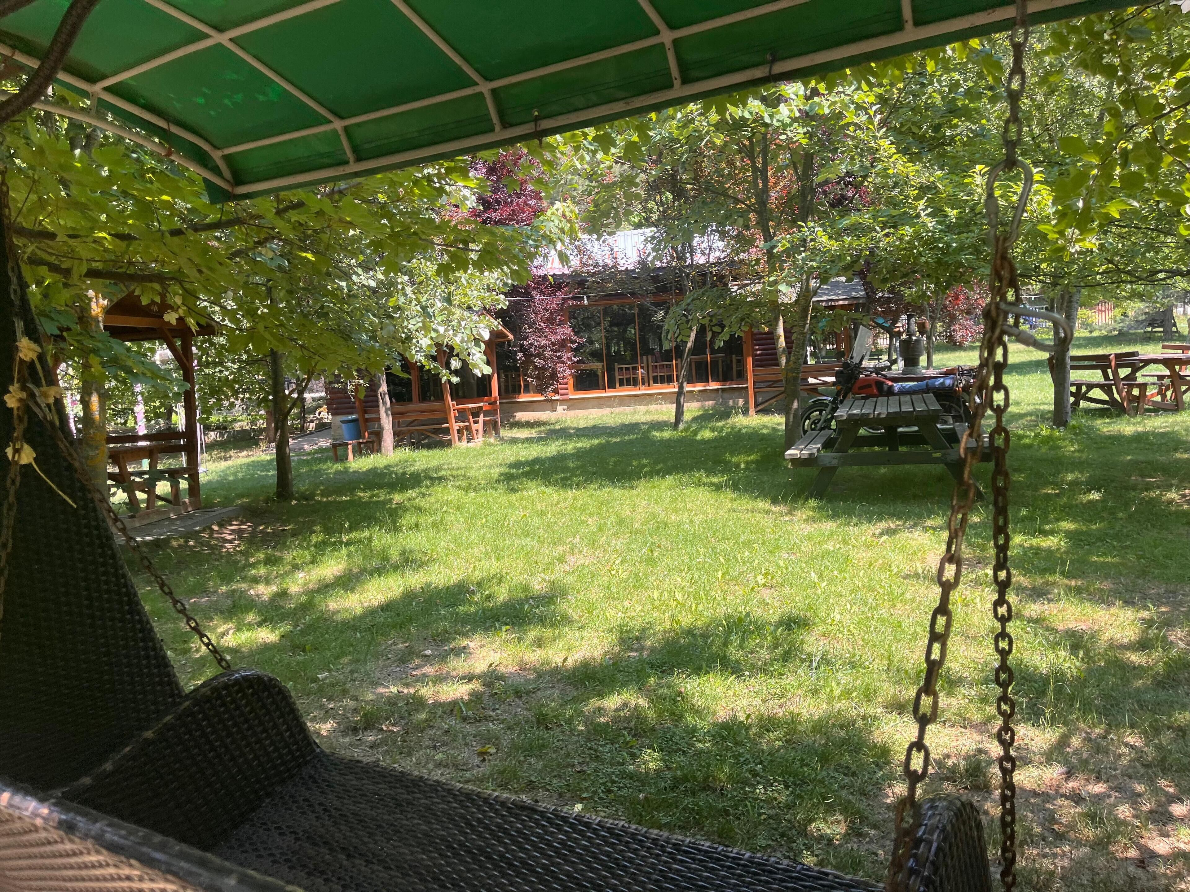 A covered outdoor seating area with a swing chair, picnic tables, and a wooden structure in the background.