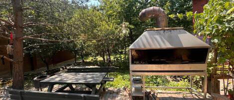 Un patio al aire libre con mesas de picnic y un horno de pizza a leña.