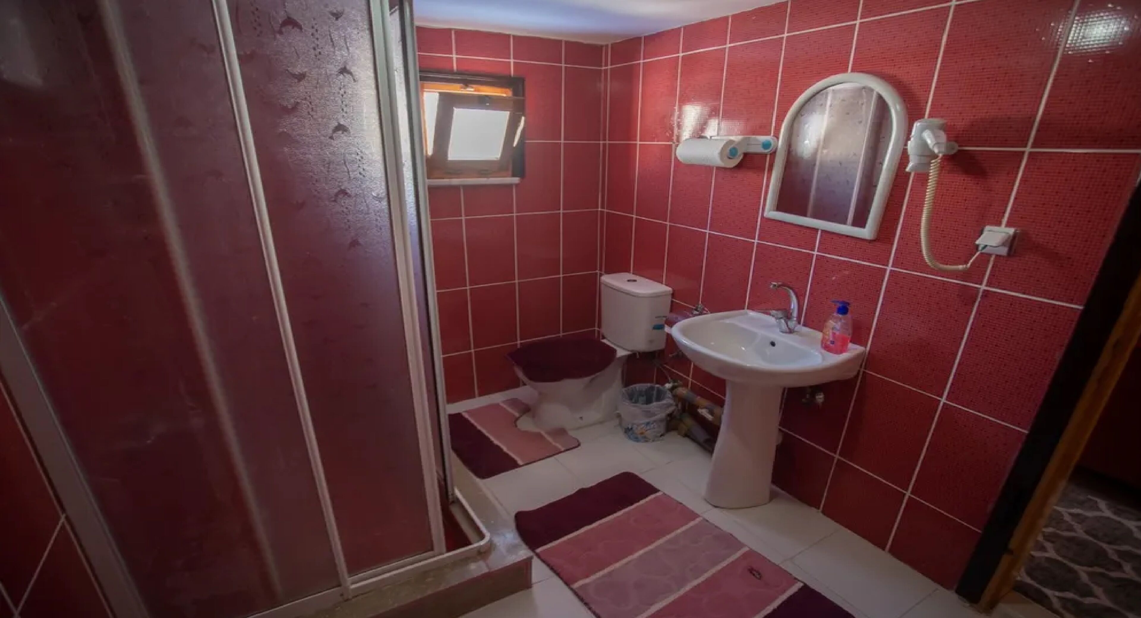 Ein Badezimmer mit roten Fliesen, einem Waschbecken, einem Spiegel und einer Toilette.