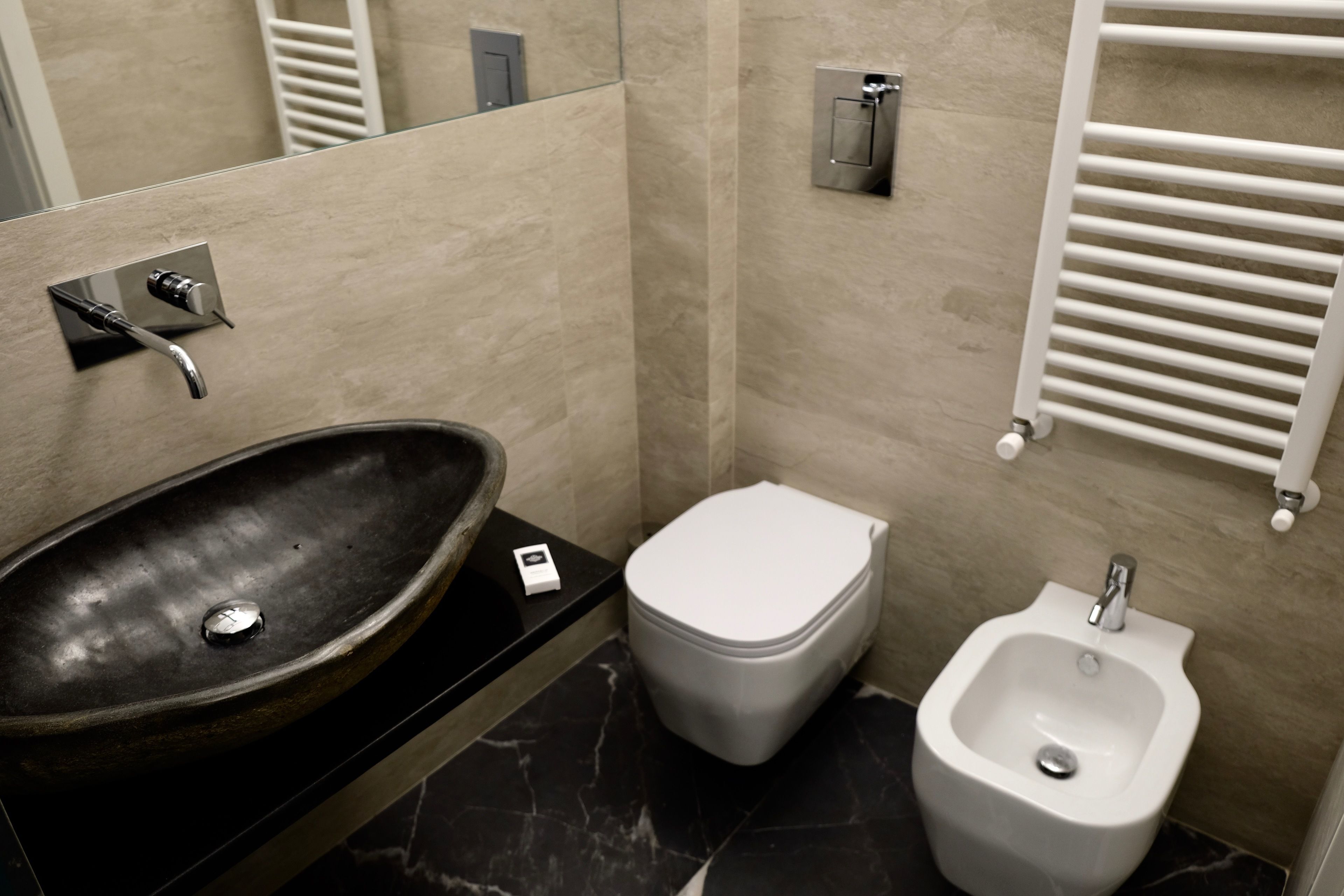 A bathroom with a black marble sink, a toilet, and a bidet.