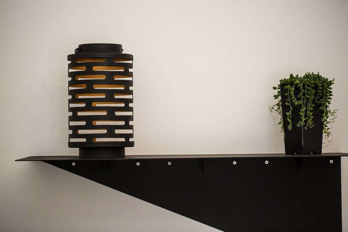 A black, modern, geometric sculpture on a black platform with a potted plant beside it.
