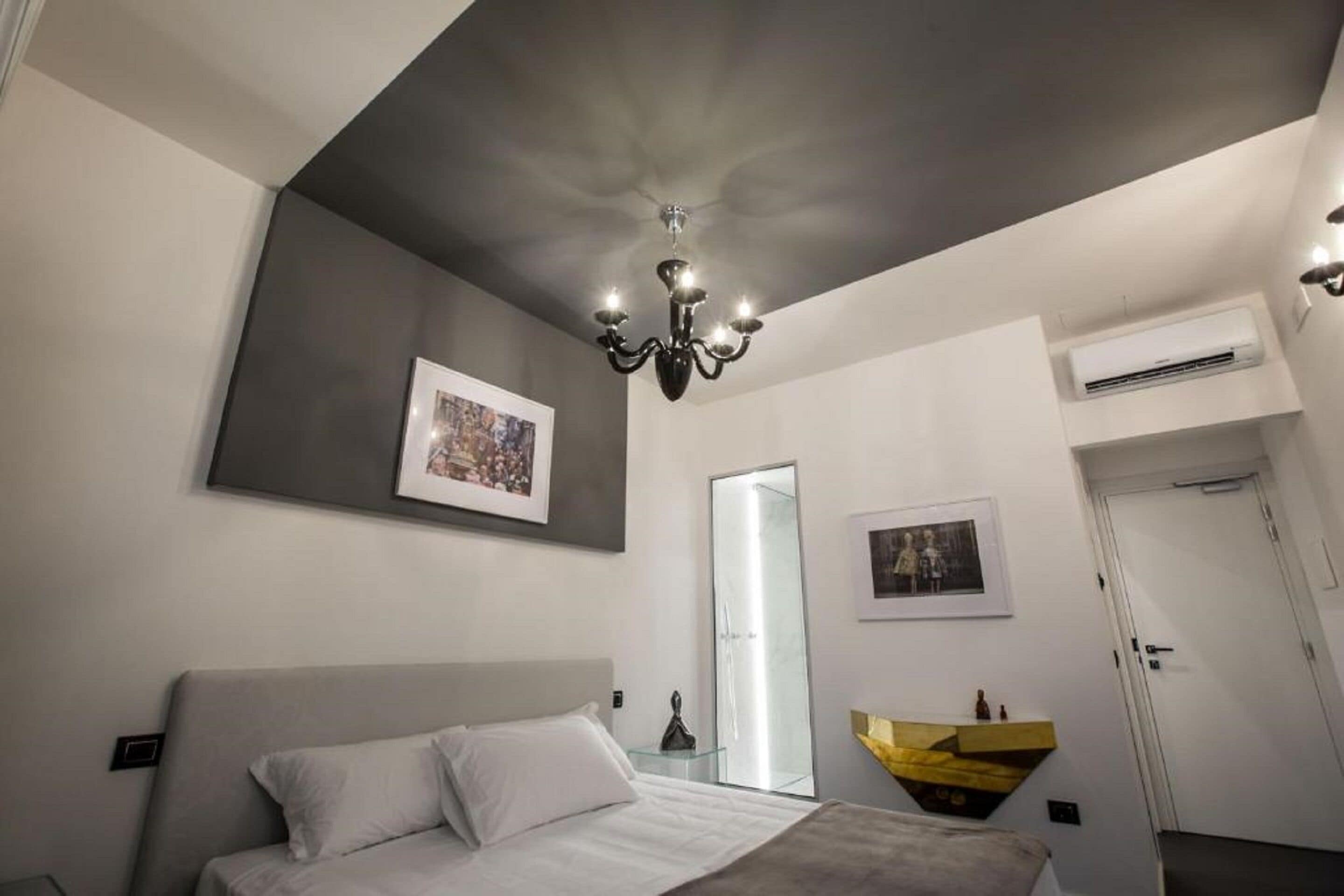 A modern bedroom with a large bed, a chandelier, and artwork on the walls.
