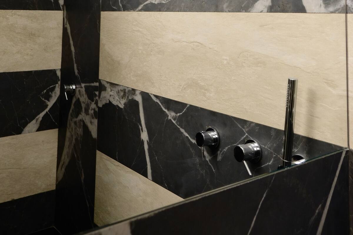 A modern bathroom with a black and white marble design, a glass shower enclosure, and a sleek faucet.