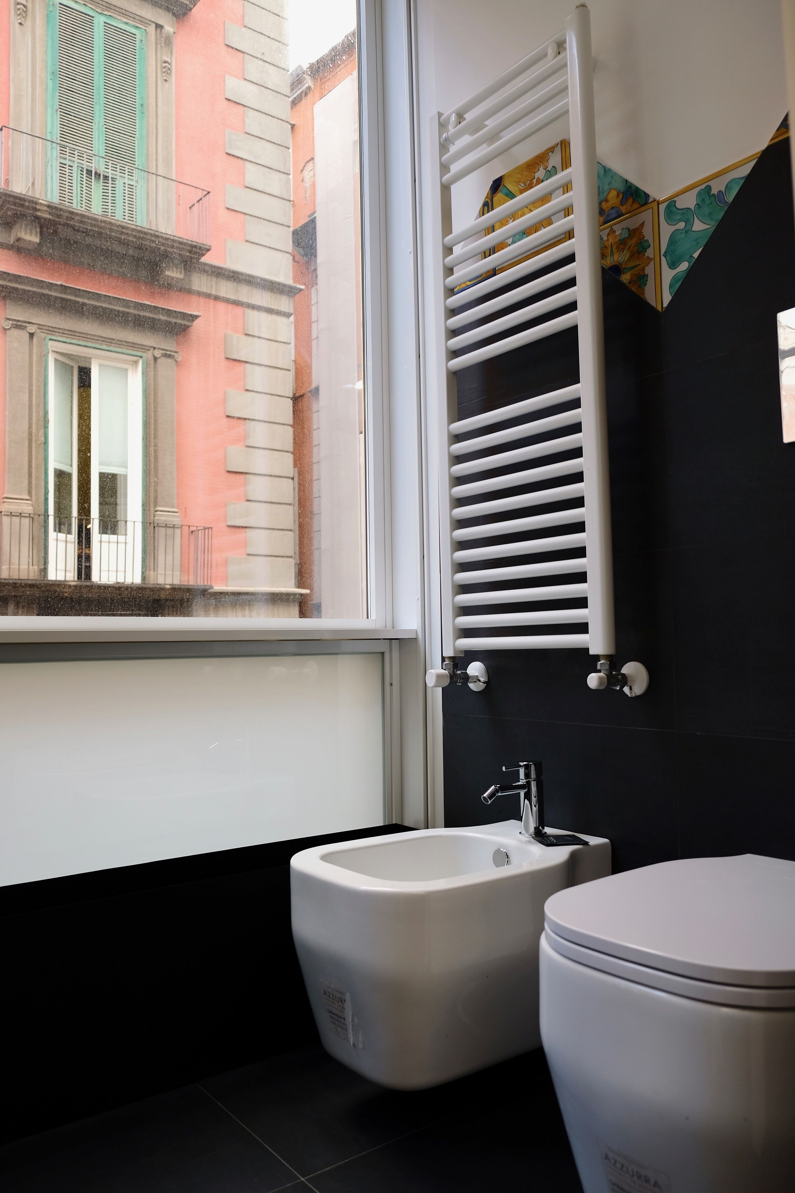 A bathroom with a bidet, toilet, and a window with a view of a building.