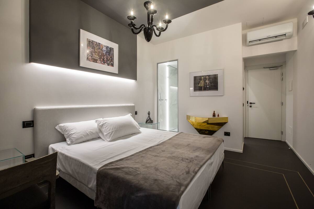 A modern bedroom with a large bed, bedside tables, a glass cabinet, and a chandelier.