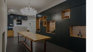 A modern kitchen with dark cabinetry, a wooden dining table, and built-in shelves with decorative items. - The Boutique Napoli Suite (Naples)