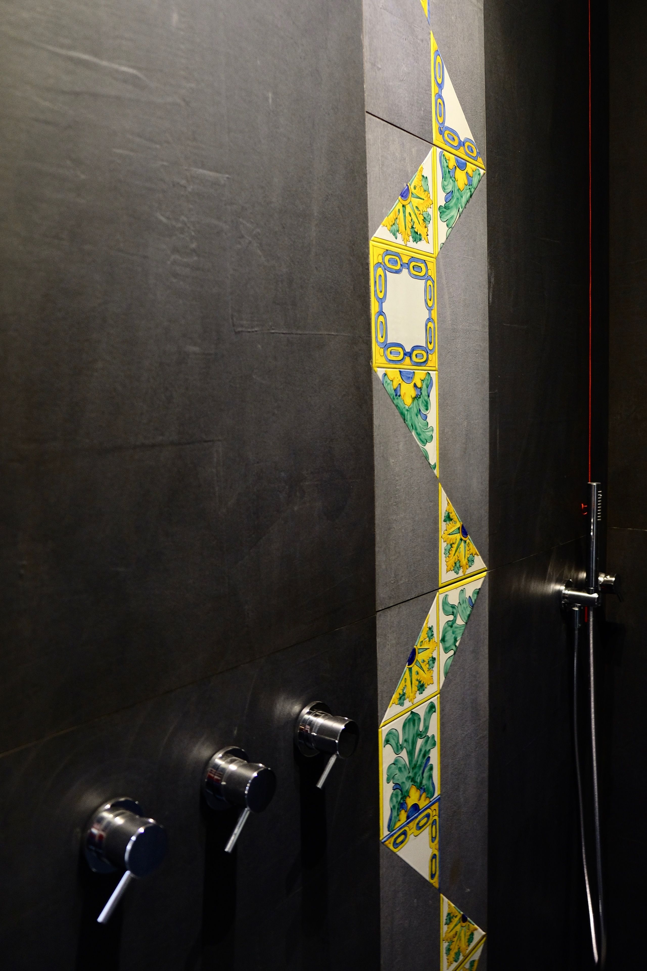 A bathroom with dark walls, a tiled accent wall, and three towel dispensers.