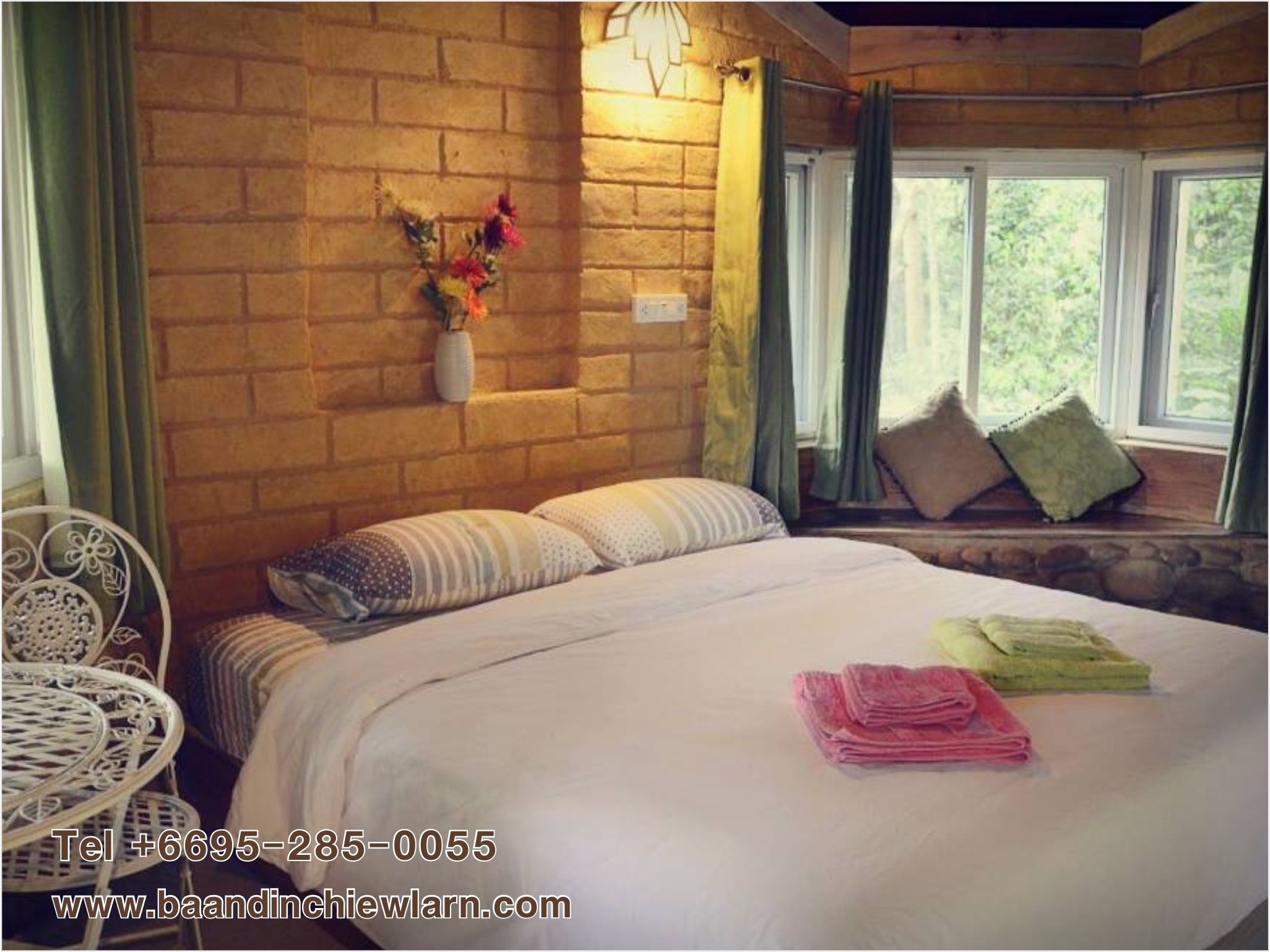 A cozy room with a brick wall, a bed with pillows, a window with curtains, and a small table with a vase of flowers.